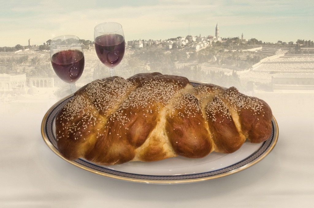 Homemade challa bread on plate with wine glasses on table fading to Jerusalem skyline in background