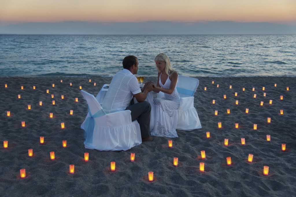 lovers couple share a romantic dinner with candles on sandy sea beach during sunset