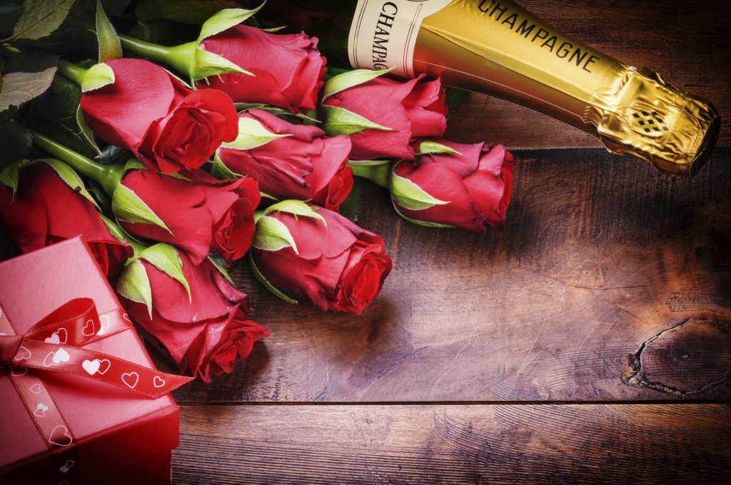 Valentine's setting with red roses, champagne and gift on old wood background