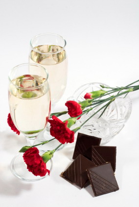 two glasses of champagne or white wine with crystal vase, carnation and chocolate tiles. White background with copyspace